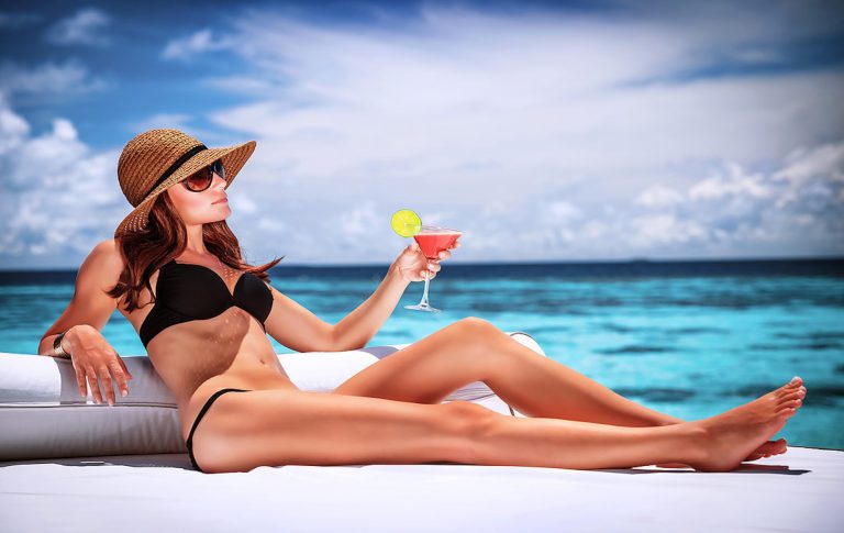 Sexy woman relaxing on luxury beach resort, sitting on lounger and drinking cocktail, summer vacation concept